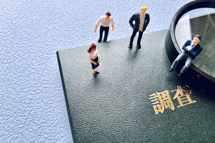 調査報告書と虫眼鏡、ビジネススーツ姿の人形たちが並ぶ探偵業のイメージ